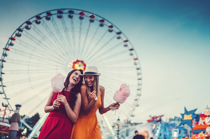 Two friends eating cotton candy and laughing at the amusement park.