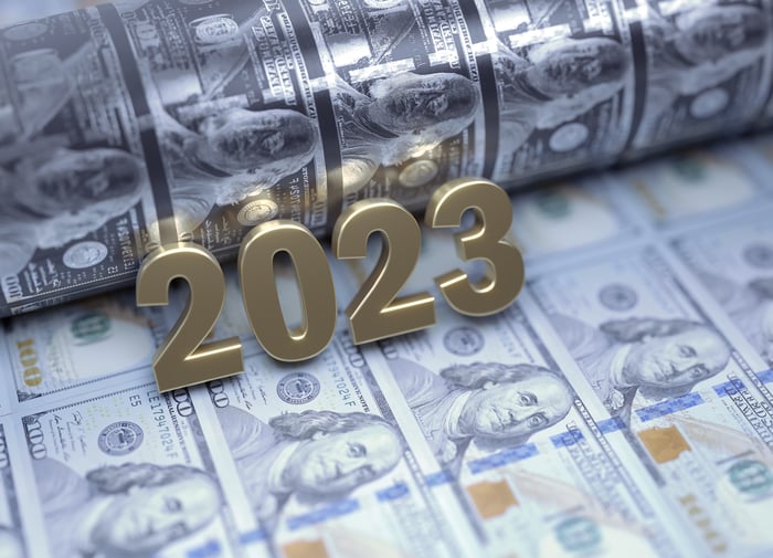 Gold-colored numbers spelling out 2023 that are placed atop one hundred dollar bills fresh out of a printing press.