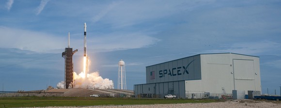 Falcon 9 rocket launch with SpaceX hangar in the foreground.