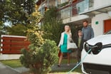 A family of 3 near an electric car.