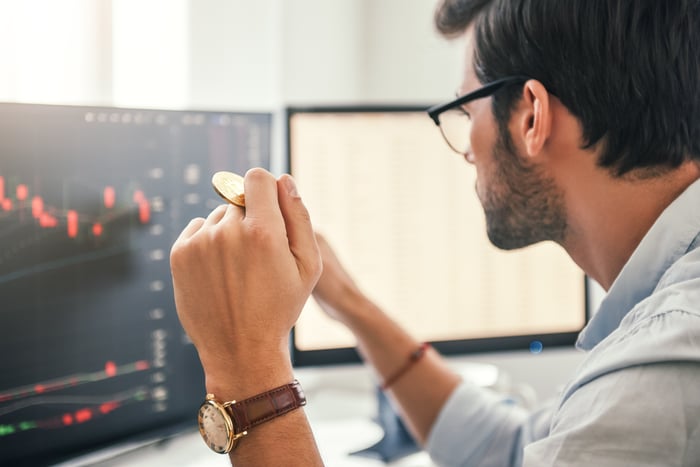 A person looking at trends on a computer with a coin in their hand.