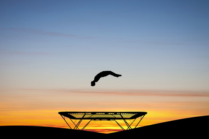 A silhouette of a gymnast bouncing off a trampoline at sunset.