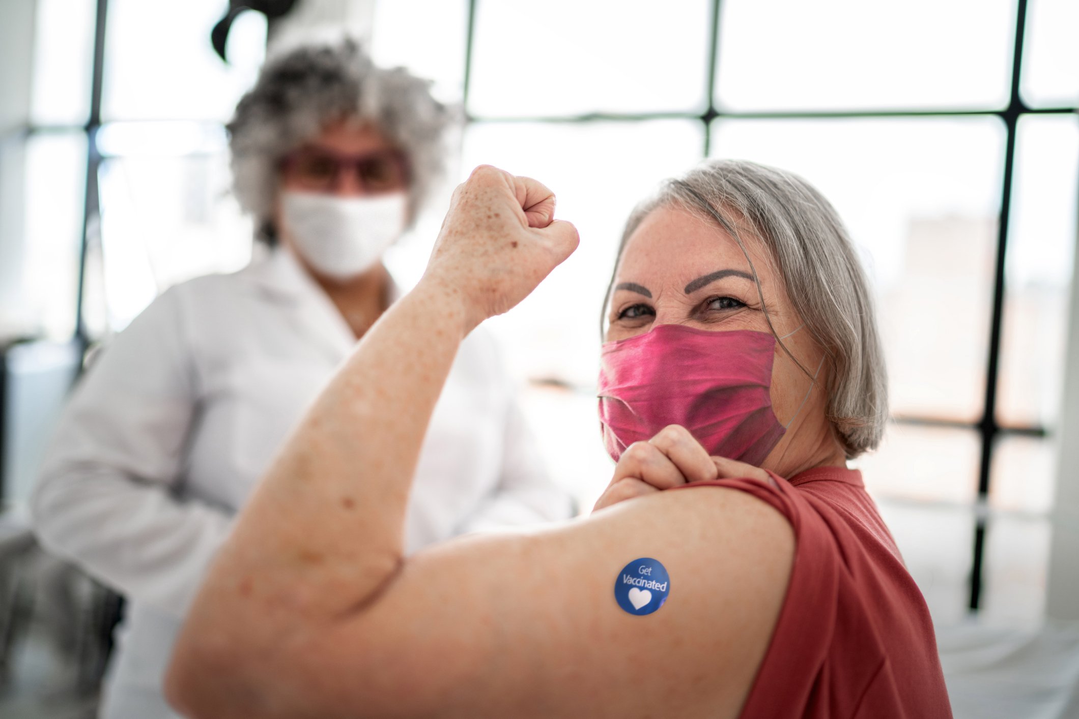 Vaccinated senior woman flexing biceps muscle with 'Got vaccinated' sticker