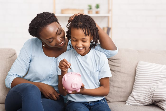 Parent and child putting money in piggy bank. 