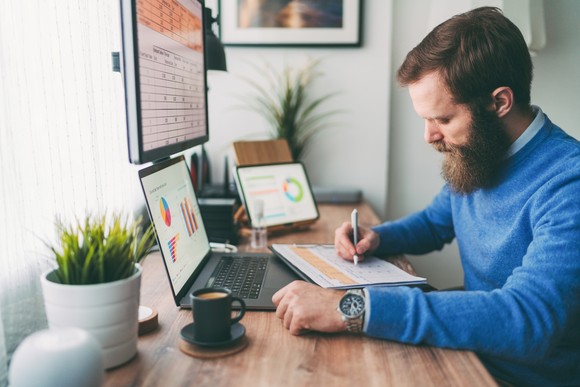 Bearded person sitting in front of computer writing a note.