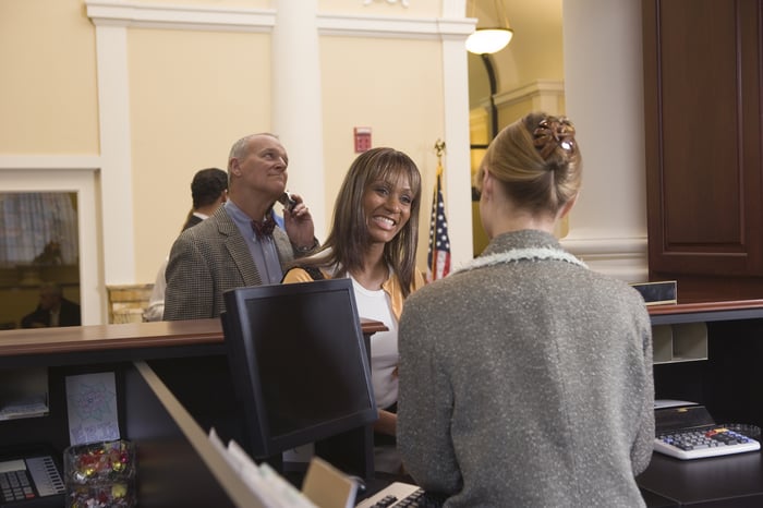 A bank teller providing service to a customer with a line behind them.