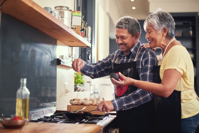 Two people adding spices to cooking food.