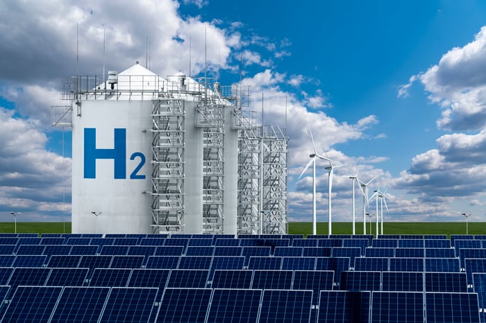 Hydrogen storage silos on a landscape with solar panels and wind turbines.