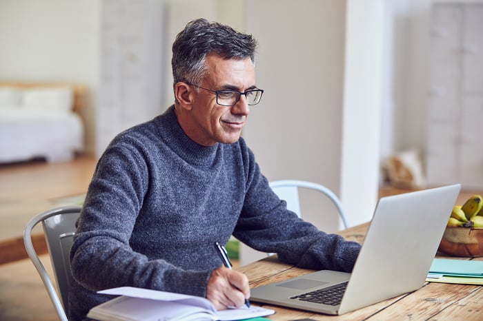 A person at a laptop holding a pen.