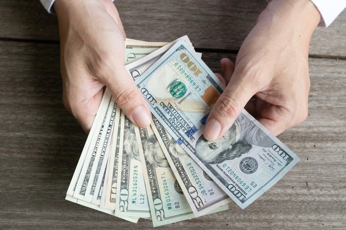 A person holding a fanned assortment of cash bills in their hands.