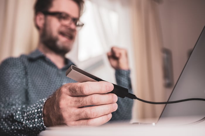 Person holding hardware device plugged into computer.