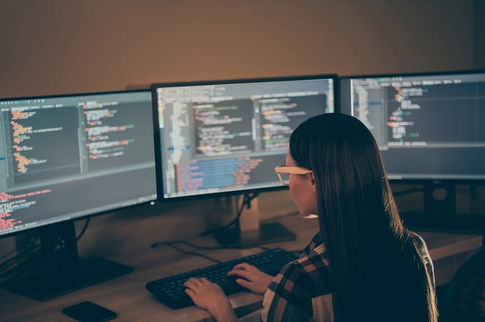A person writing code while sitting at a desk with multiple computer monitors.