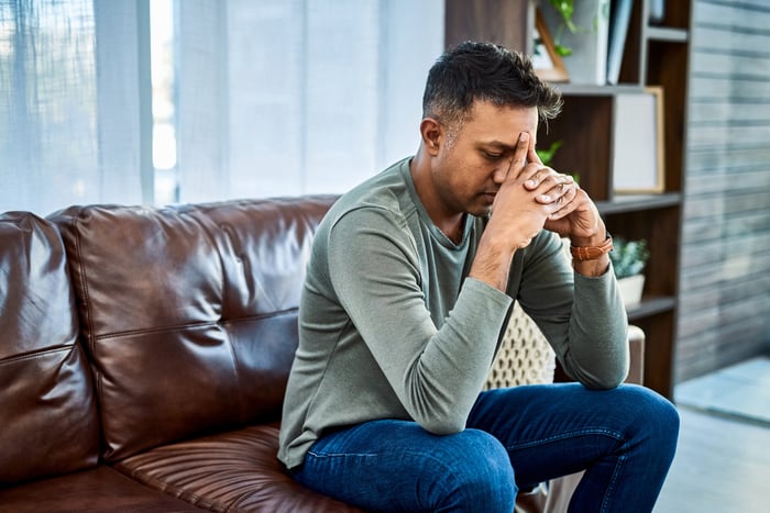 A person sitting on a couch with eyes closed and hands on forehead.
