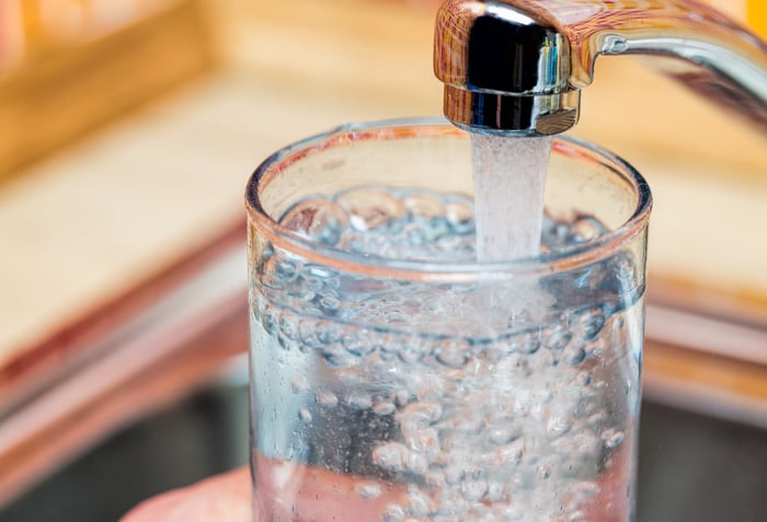 A person filling up a glass of water from a kitchen sink faucet.