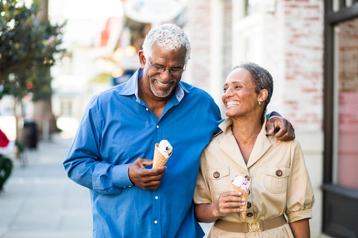 A couple is walking outdoors, smiling, with ice cream cones.