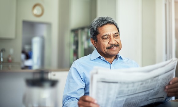 A person reading a financial newspaper while seated in their home.
