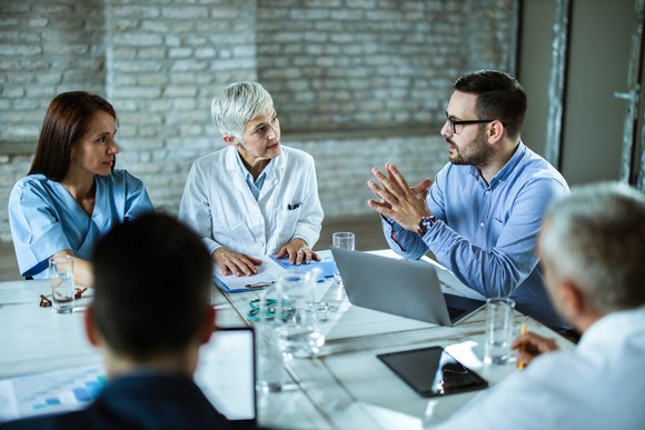 An investor talks with several doctors and healthcare staff in a meeting room.