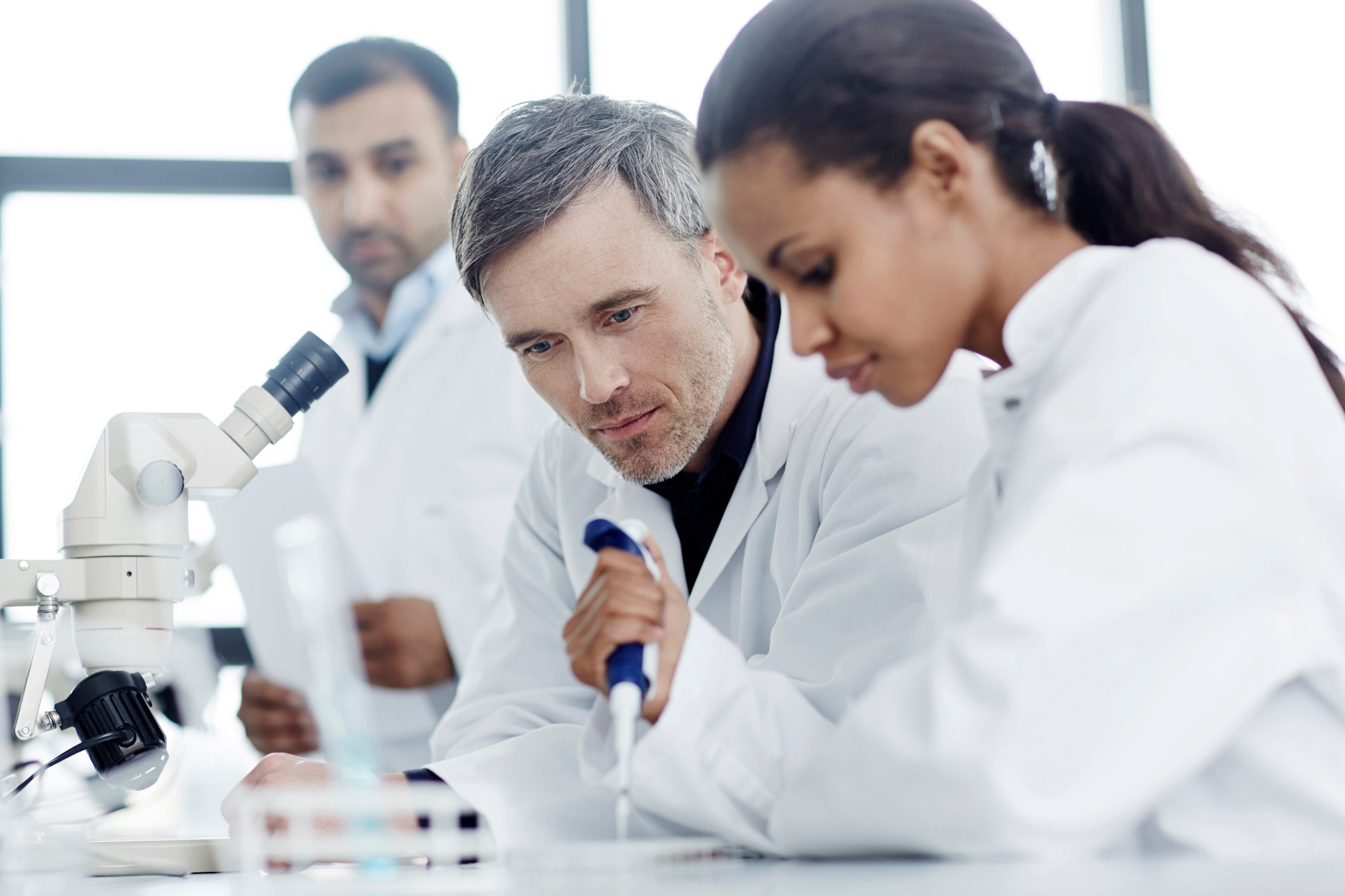 scientist pipettes while two others watch in a lab
