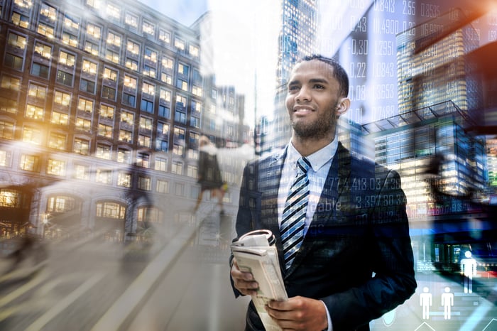 Businessperson standing on a city street holding a newspaper.