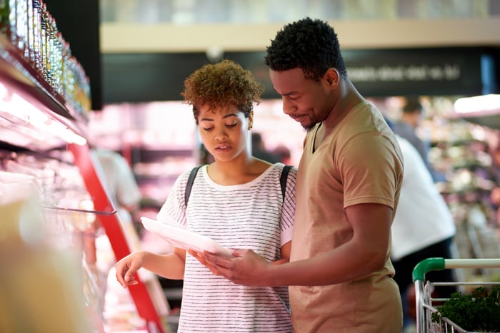 Two people looking at a package of meat in a grocery store.