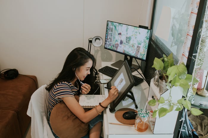 A smiling person wearing earphones and drawing on a tablet.