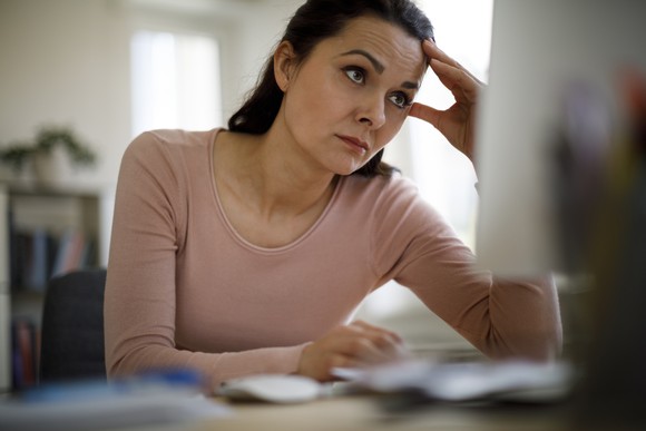 A person with hand held to head looking at a computer screen.