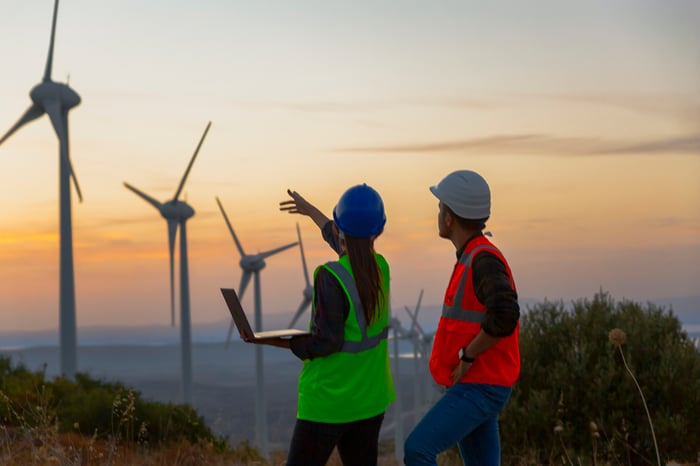 Two workers in hard hats looking at a row of wind turbines.