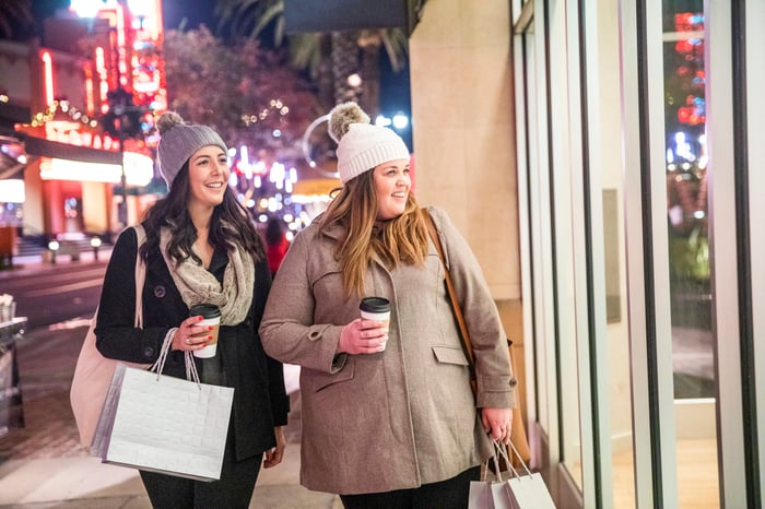 Two women with bags looking in a store window.