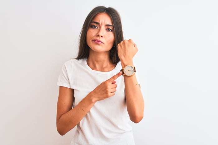 A person pointing to a wristwatch.