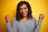 Happy person with fists in front of a yellow wall.