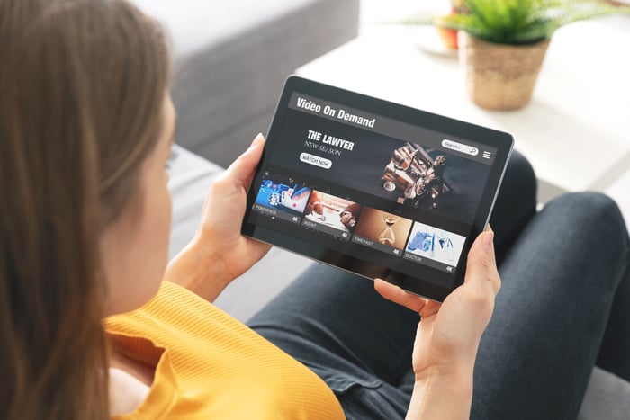 A person sitting on their couch who's using a tablet to watch streamed content. 