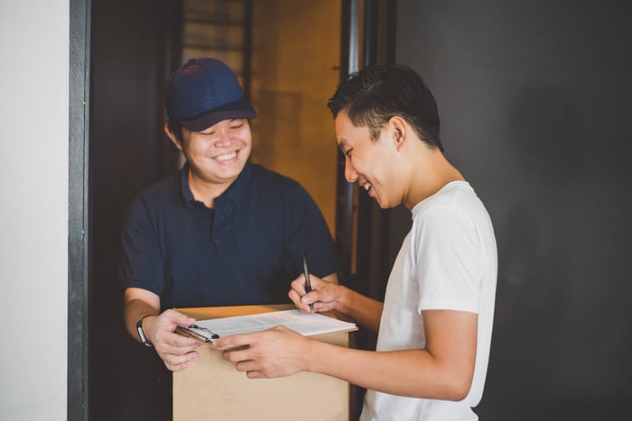 A smiling courier driver delivering a package to a smiling customer. 