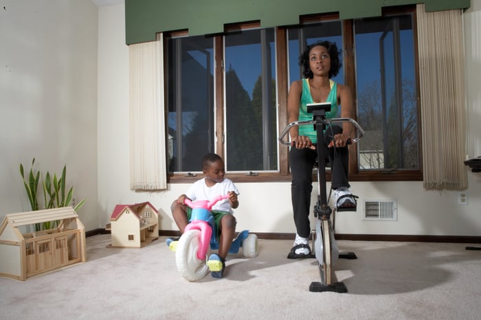 A person on a stationary bike with a child playing next to them.