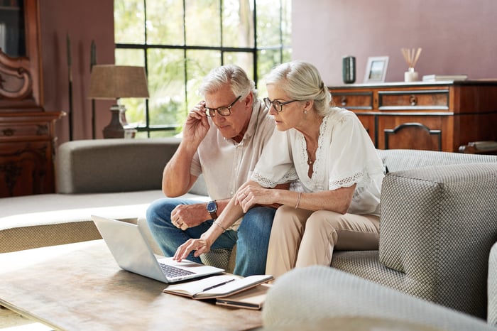 A couple sits on a couch while looking at a laptop.