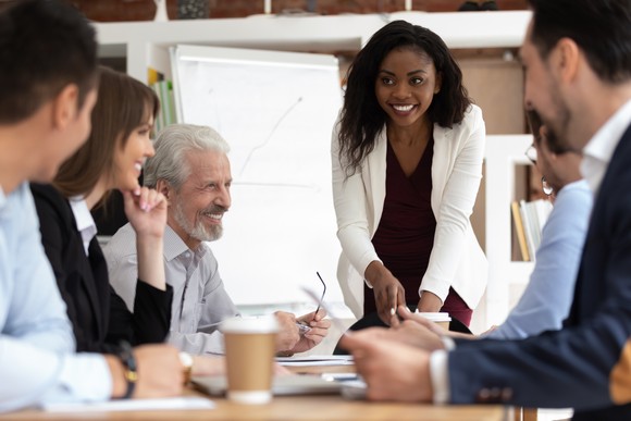 An investor stands at the foot of a conference table while presenting to her coworkers.
