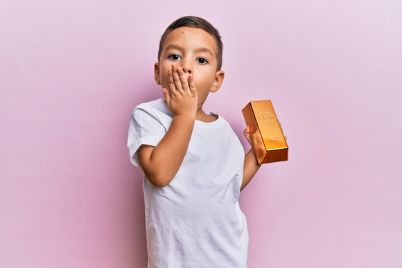 Toddler holding gold bar and covering their mouth.