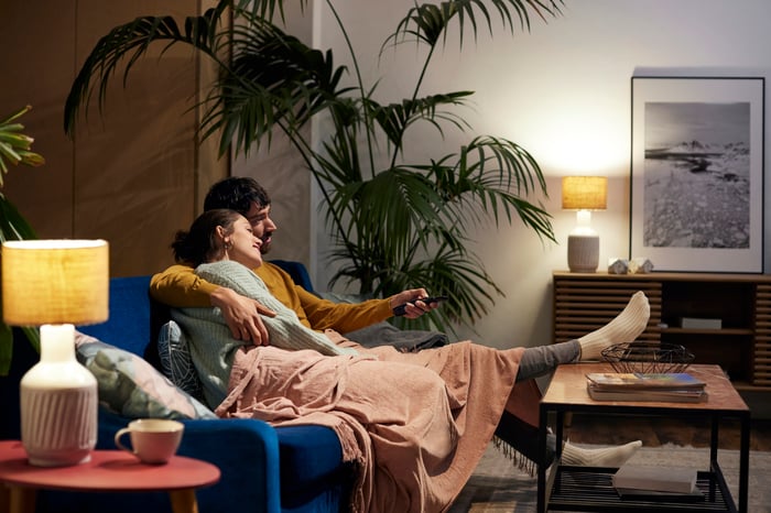 A young couple cuddling on a loveseat watching television. 