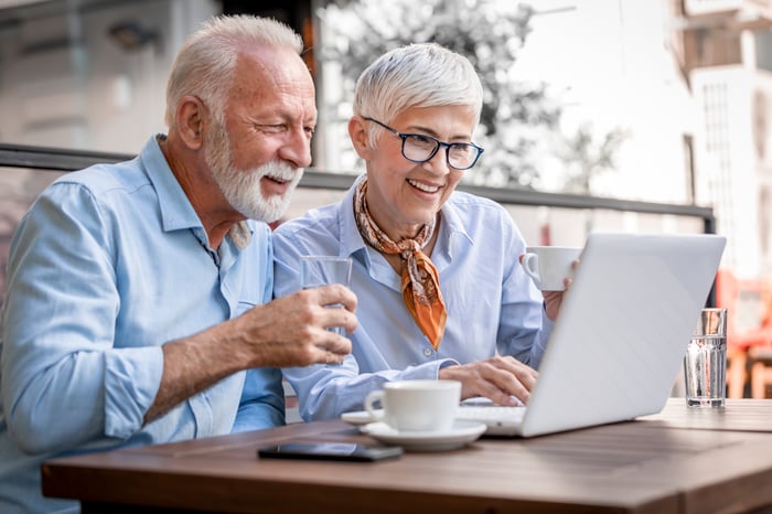 Two people sit at a table while drinking coffee and looking at a computer.