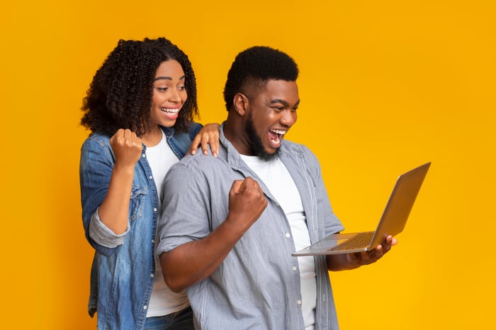 A happy couple checks a portfolio on a laptop.