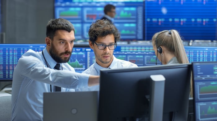 Traders on Wall Street looking at trading terminals with stock quotes in the background.