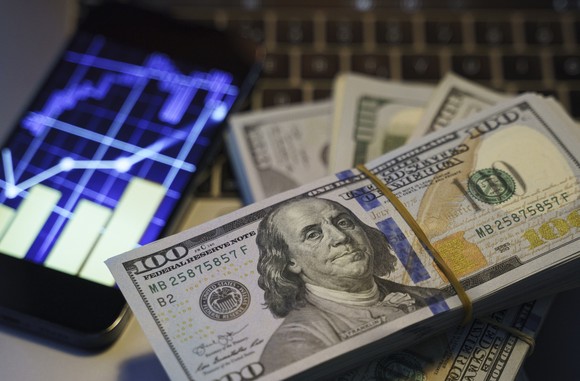 $100 bills next to a smartphone with a stock chart.