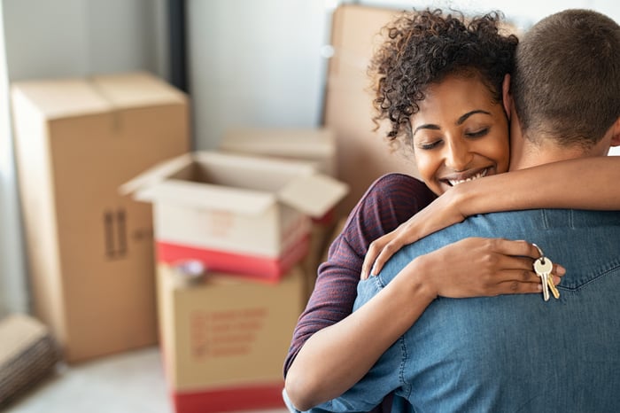 Two people hugging, one holding new house keys, in front of moving boxes.