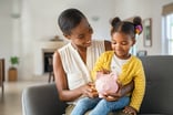 mother teaching daughter how to save money in piggy bank