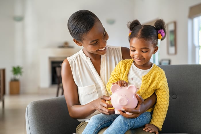 A mother teaches her daughter to save money in a piggy bank.