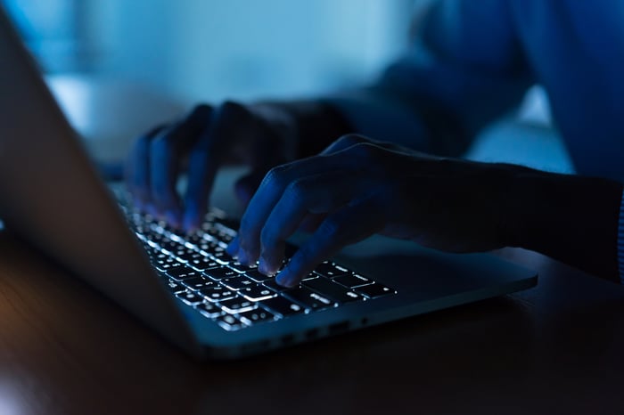 A person typing on a laptop with backlit keys in a dimly-lit room. 