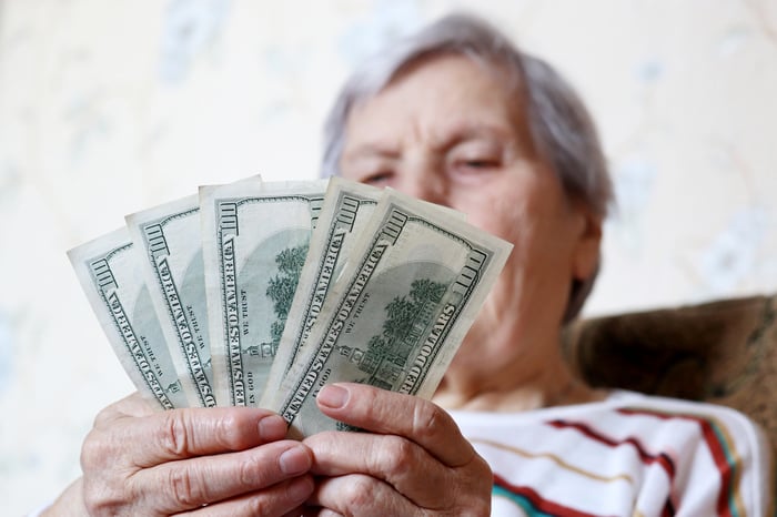 A person holding five fanned one-hundred-dollar bills in their hands. 