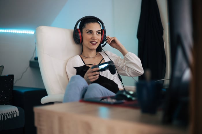 A young person wearing a headset and holding a gaming controller smiling.