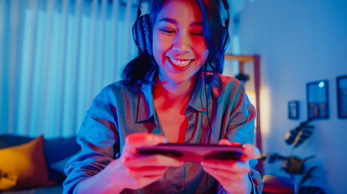 A smiling person with headphones on plays a mobile game at home.
