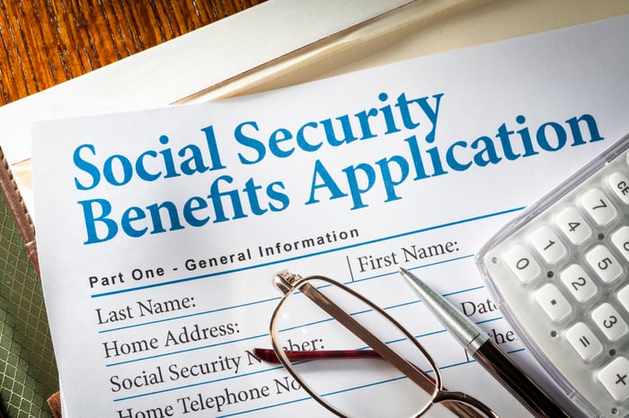 A pair of glasses, a pen, and a calculator set atop a Social Security benefits application. 