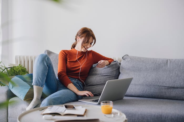 A person on the couch keying credit card information into a laptop.